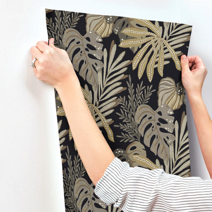 Gold and taupe tropical leaf print on black background, poster being hung as wall decor.