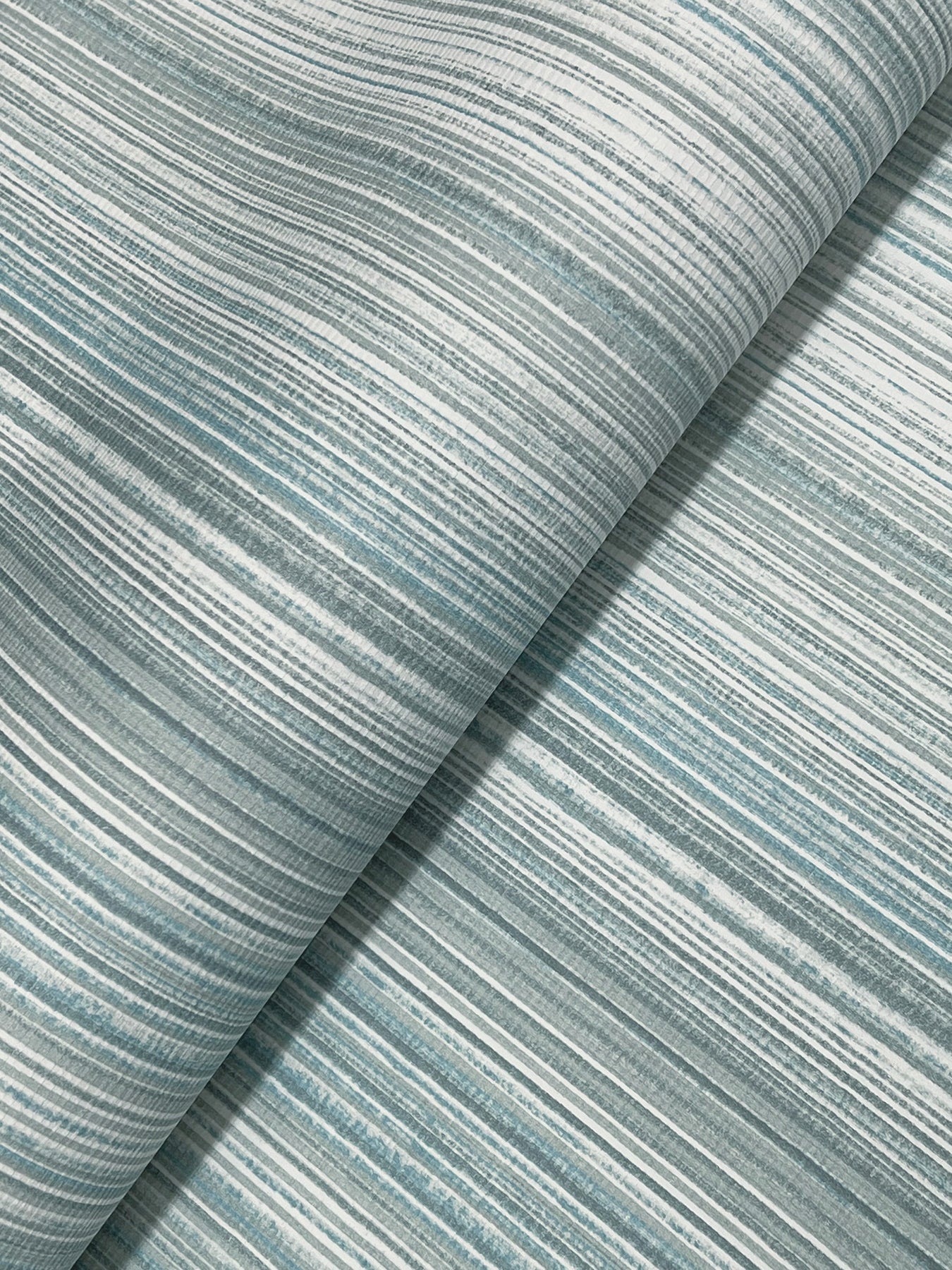 Light blue and white striped wallpaper on a roll with an ombre stripe pattern; modern blue wallpaper.