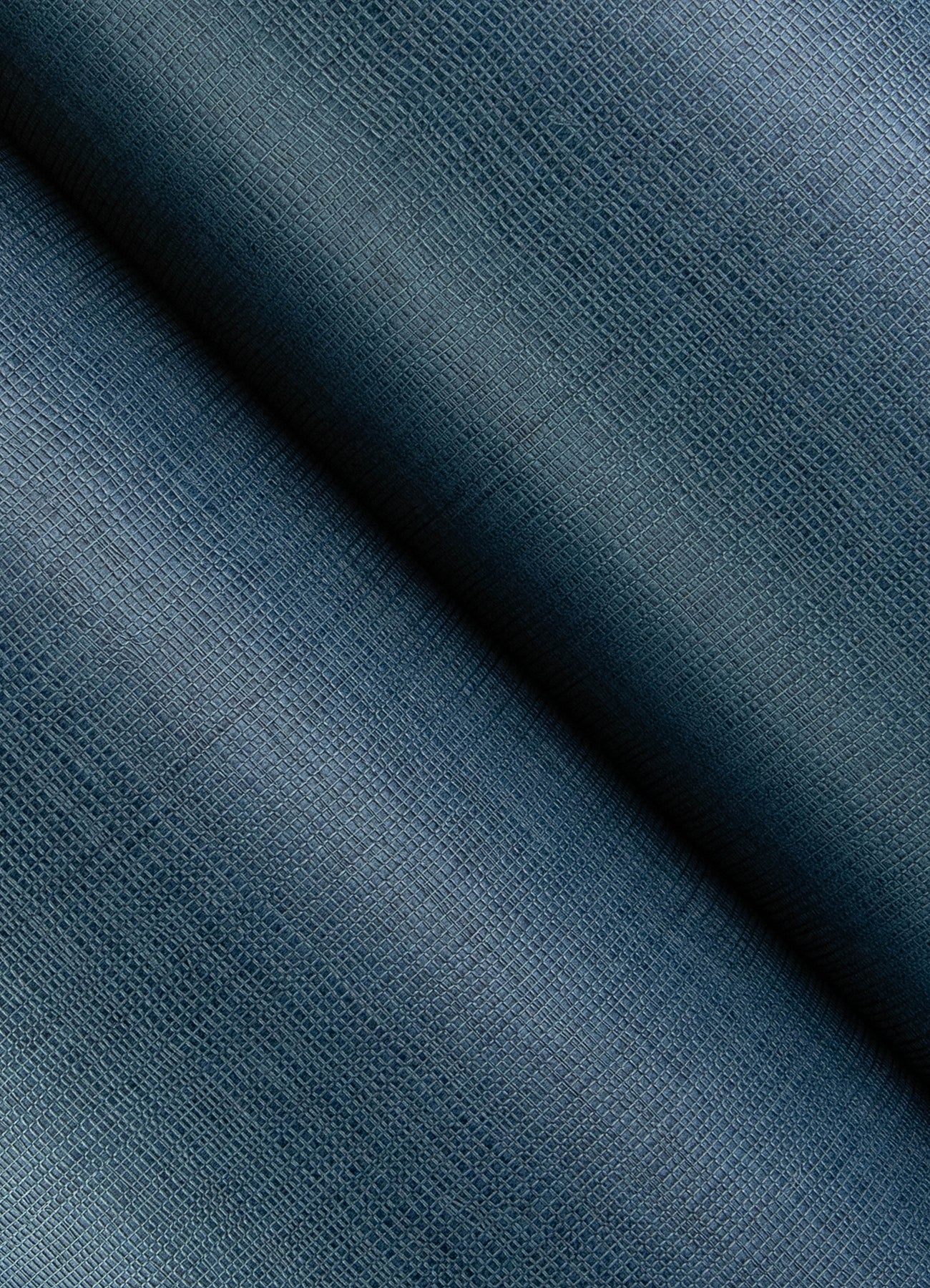 Close-up of dark blue open-weave wallpaper texture with a diagonal fold, showing a textured weave and subtle gradient.