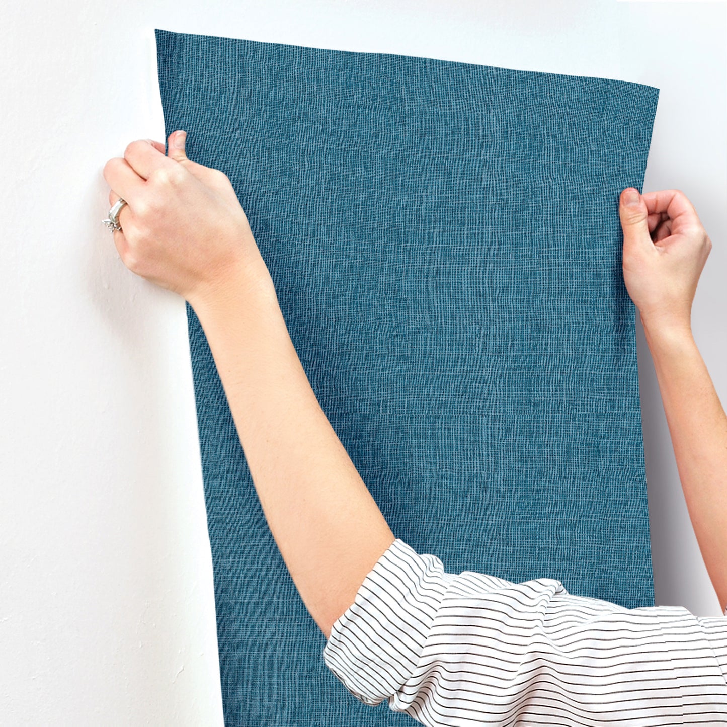 Two hands hold up a blue textured fabric panel against a light wall; casual linen-like curtain or wall hanging.