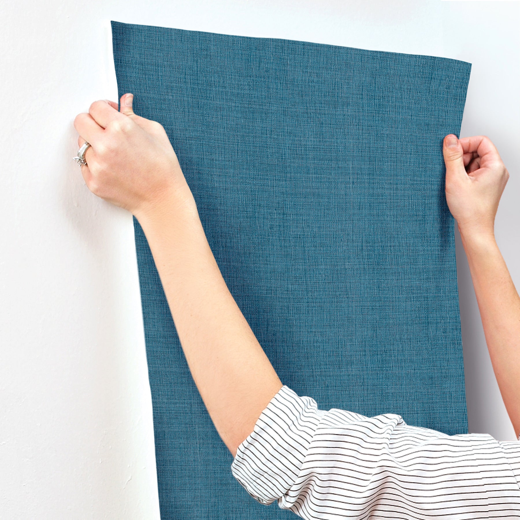 Two hands hold up a blue textured fabric panel against a light wall; casual linen-like curtain or wall hanging.