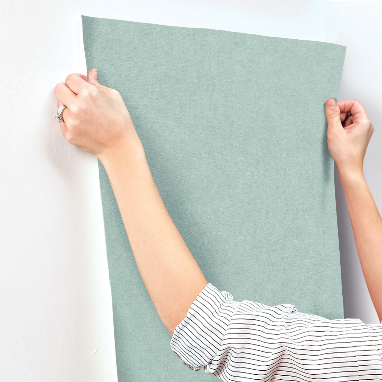 Rectangular sage-green fabric panel being stretched by hands; striped-sleeve person against a white wall.