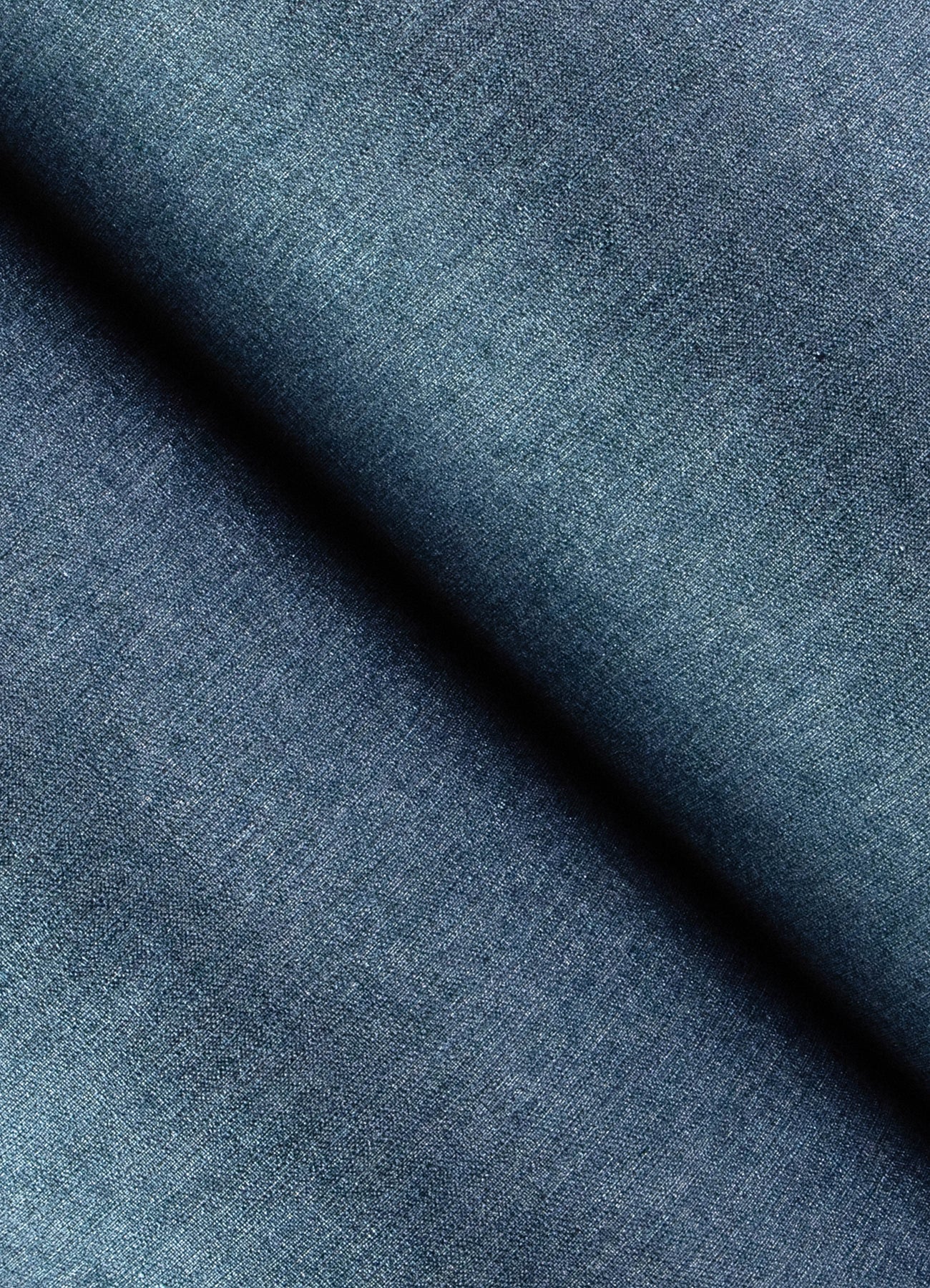 Close-up of blue denim-inspired faux linen wallpaper showing textured weave and indigo variations, with a diagonal fold.