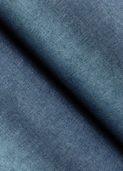 Close-up of blue denim-inspired faux linen wallpaper showing textured weave and indigo variations, with a diagonal fold.