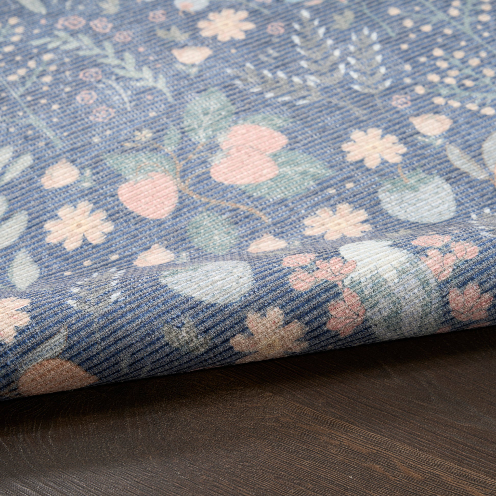 Blue floral fabric with pastel pink and white blossoms and leaves, folded on a dark wooden surface.