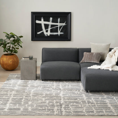Dark gray fabric sectional with chaise, beige pillows and throw, concrete side table, geometric gray rug, black abstract art.