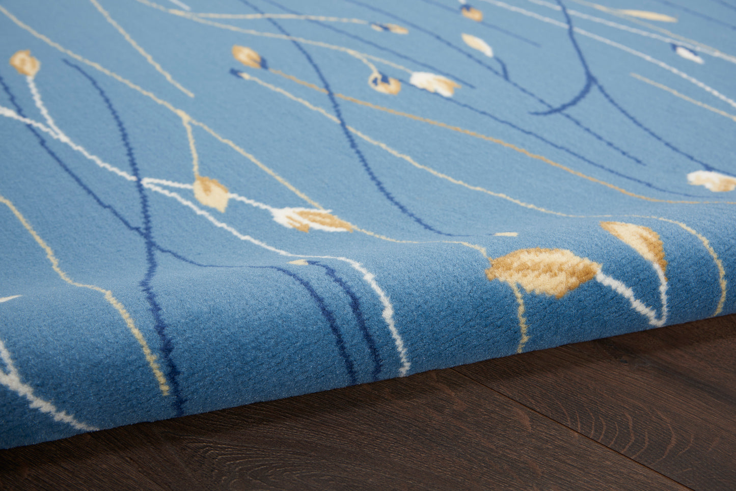 Blue plush area rug with white and mustard abstract lines on dark wood floor.