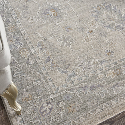 Light gray floral area rug with beige and blue accents and ornate scrollwork, shown with a gold-toned carved furniture leg.