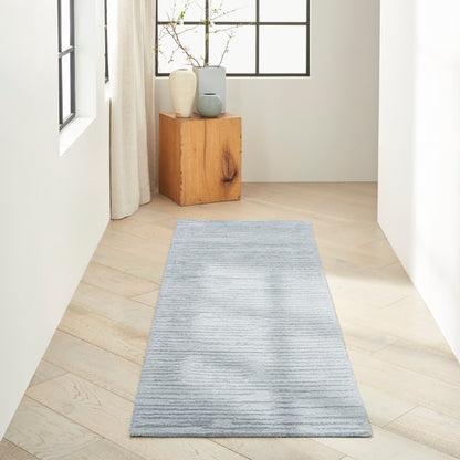 Light blue-gray striped runner rug along a pale wood floor in a bright hallway with a wooden block and vases.