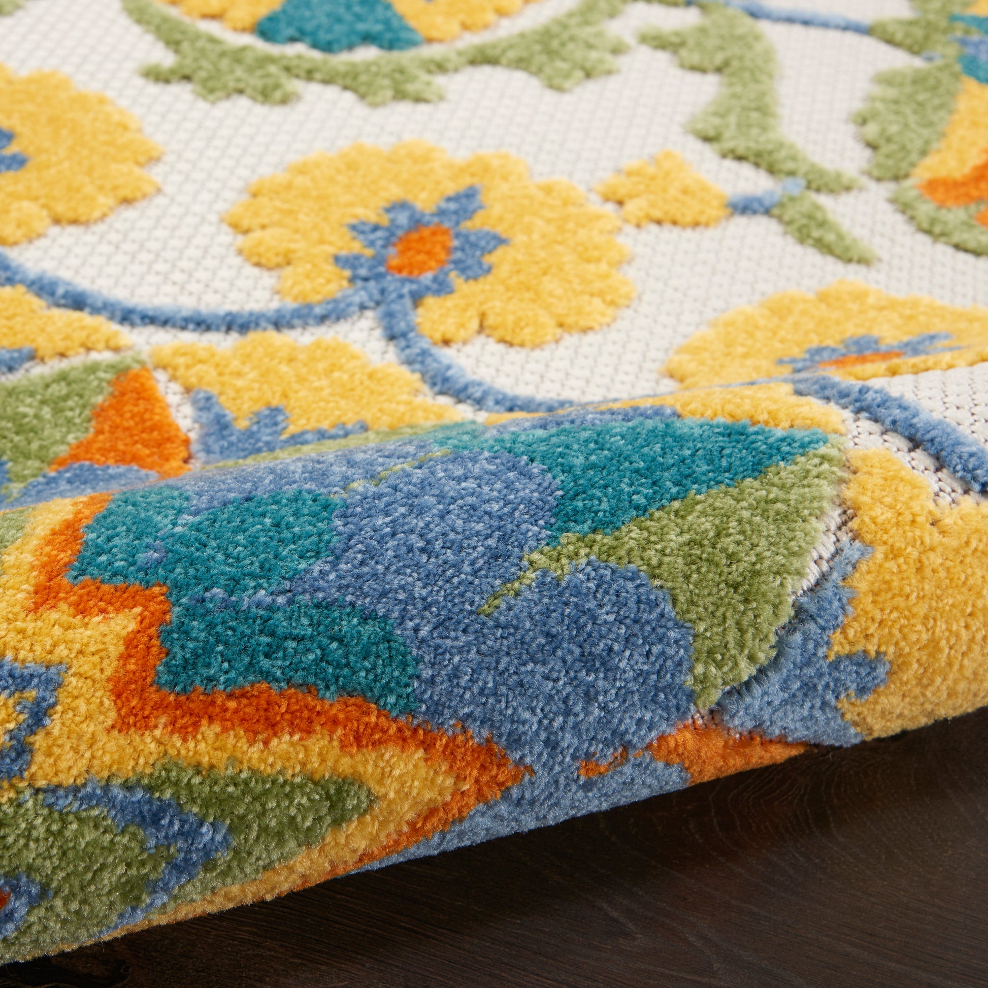 Close-up of a vibrant tufted rug with yellow floral motifs, blue, green & orange accents; thick pile and rolled edge.