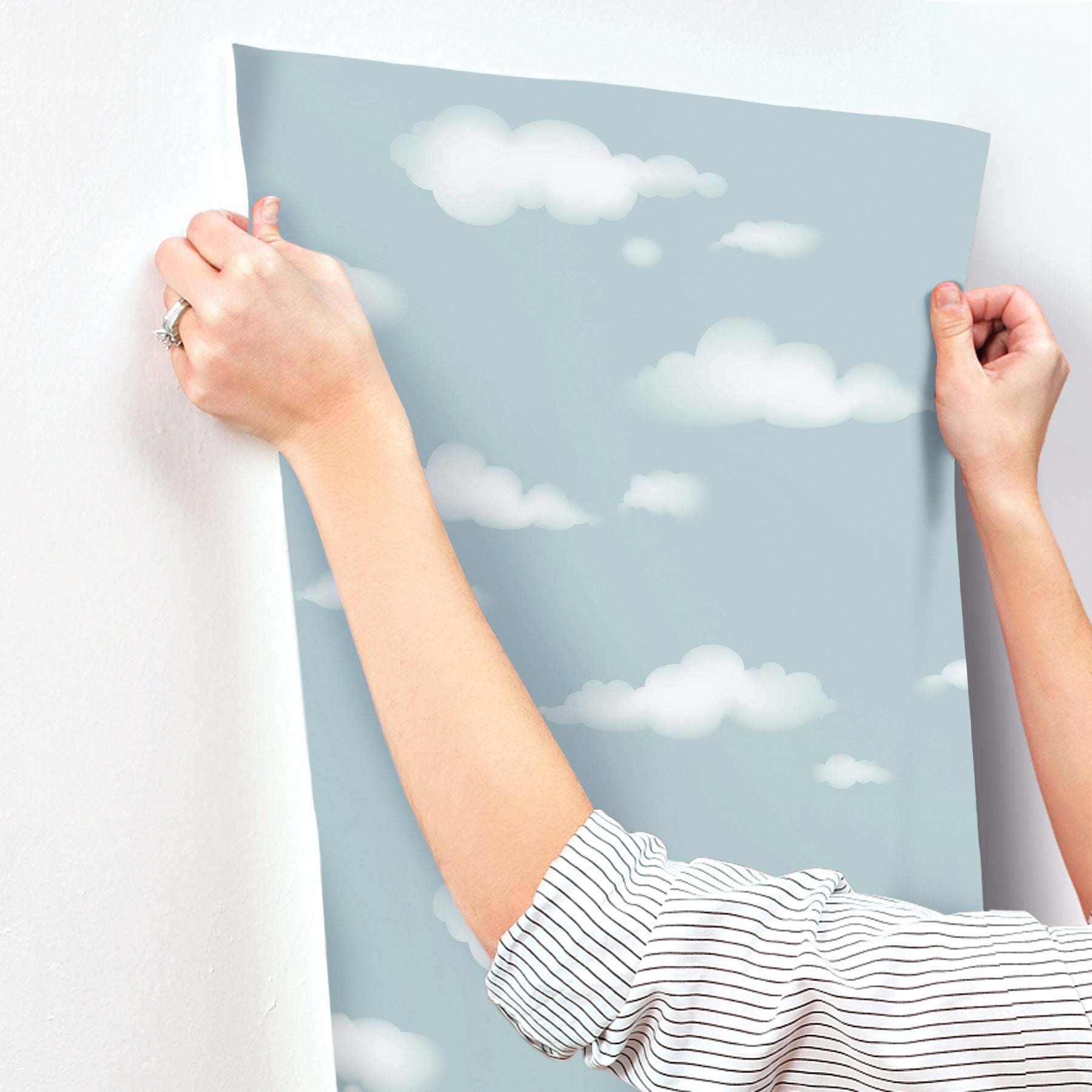 Light blue cloud-pattern wallpaper sheet held up by hands, ready to hang as airy wall decor.