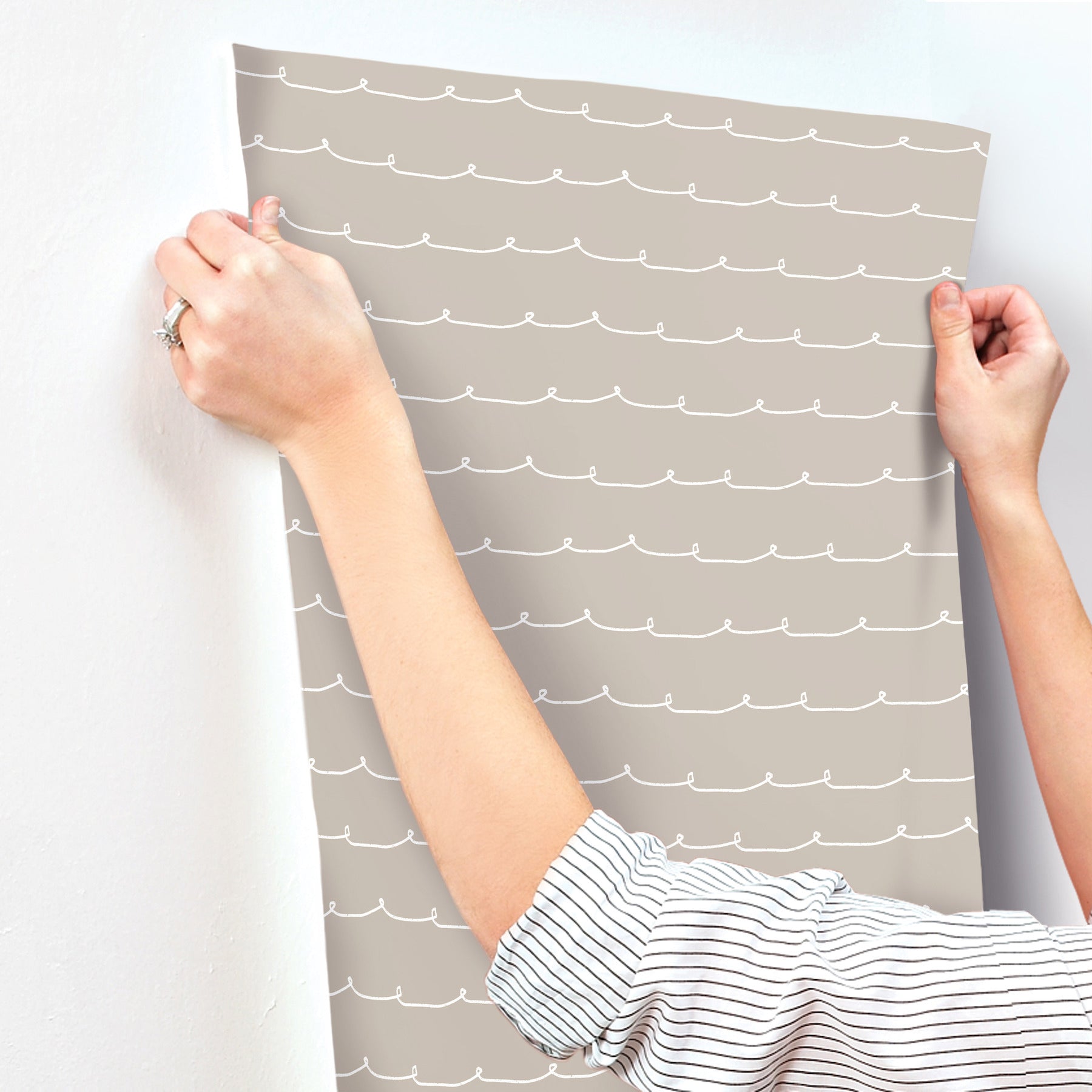 Taupe wallpaper with white wavy lines being peeled from a wall; hands in striped sleeves.