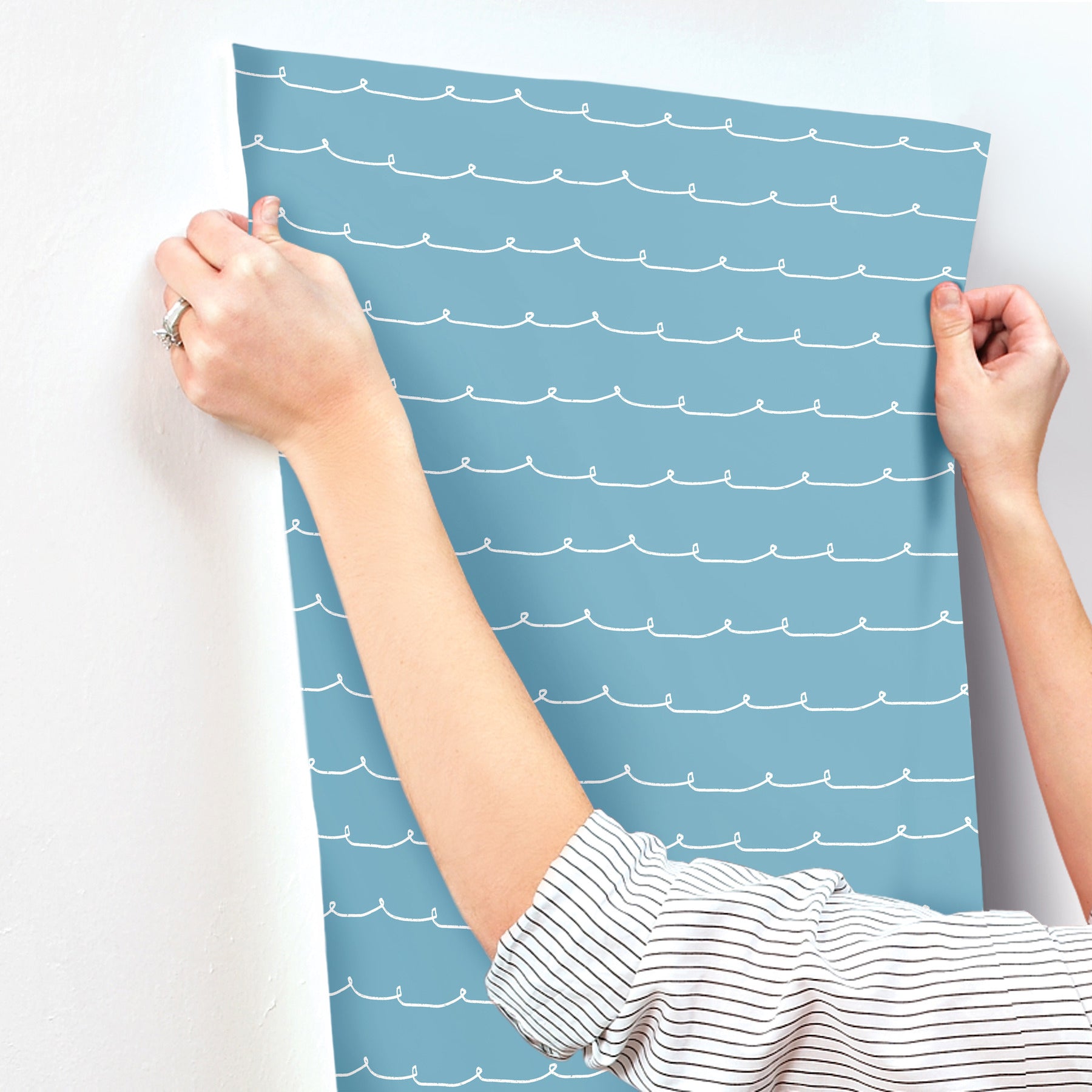 Blue striped wallpaper with white wavy lines, held up by two hands.