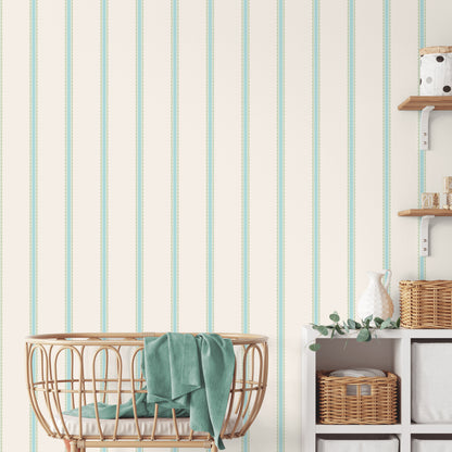 Natural rattan baby bassinet with teal blanket on cream wall with mint-striped wallpaper; wicker baskets and cubby shelves.