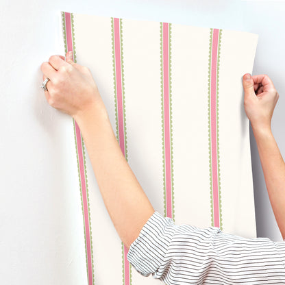Hands in a striped shirt mount a fuchsia scalloped bobbin-stripe wallpaper panel.