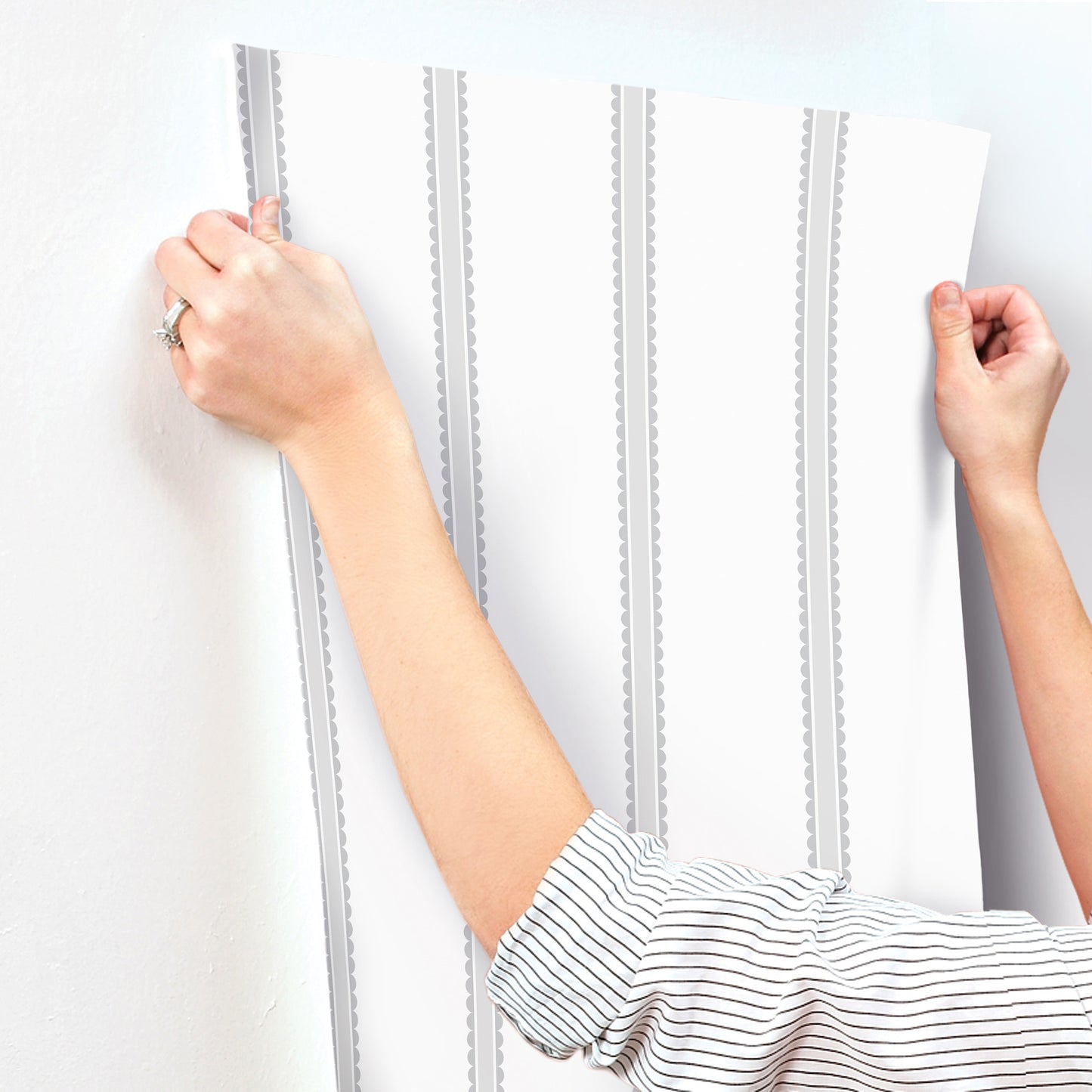 Hands press white vinyl wallpaper panel with grey vertical stripes onto wall.