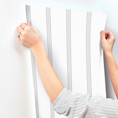 Hands press white vinyl wallpaper panel with grey vertical stripes onto wall.