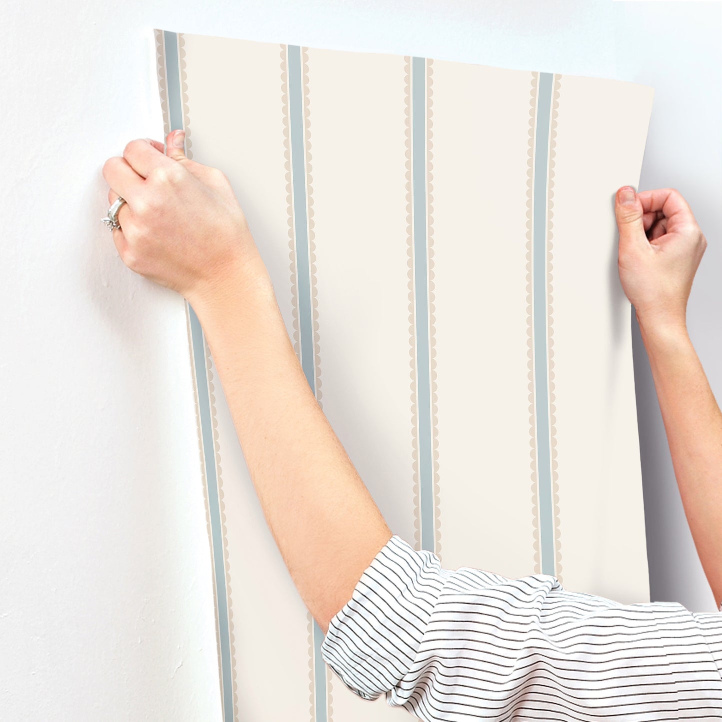 Beige wallpaper panel with pale blue vertical stripes and dotted trim, held by two hands.