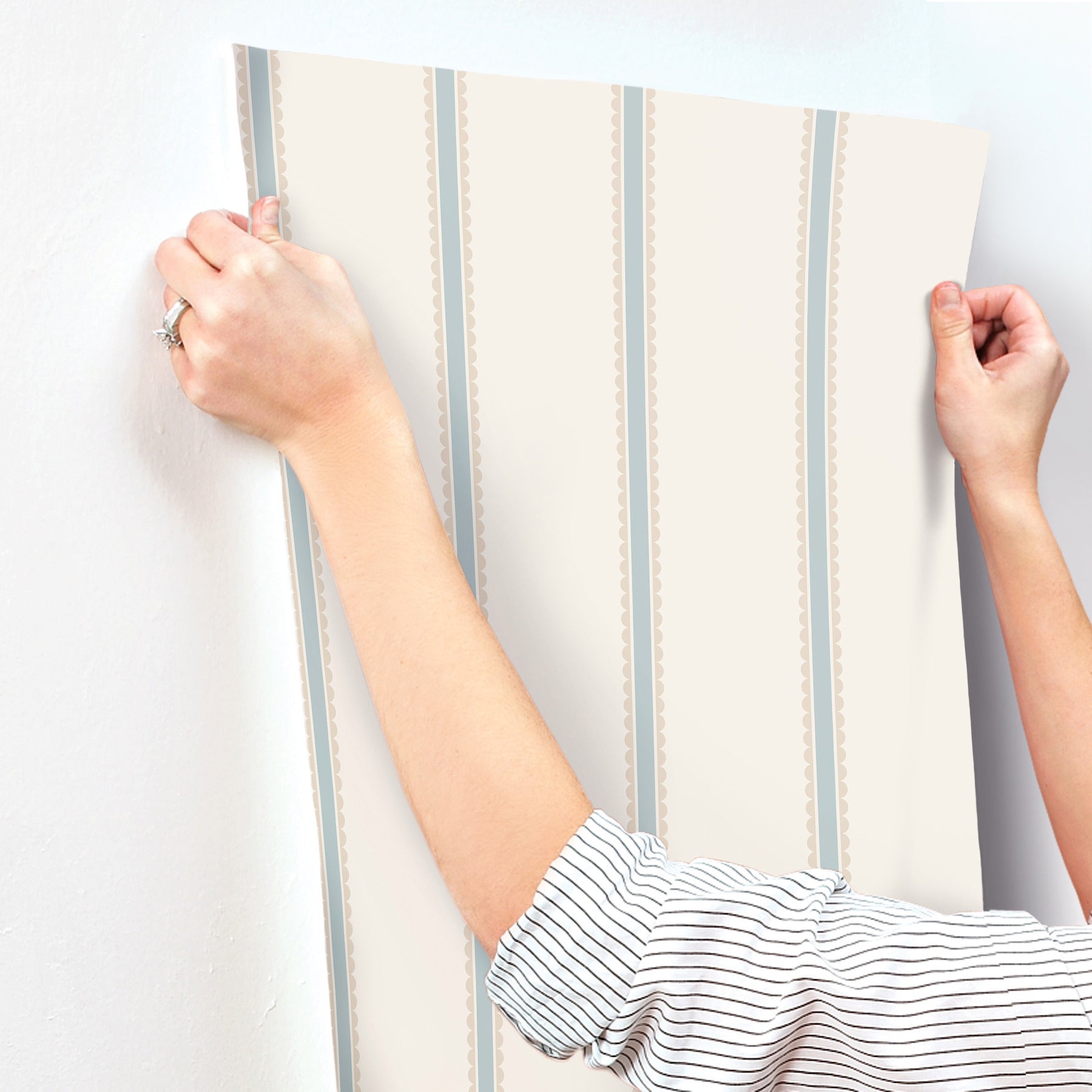 Beige wallpaper panel with pale blue vertical stripes and dotted trim, held by two hands.
