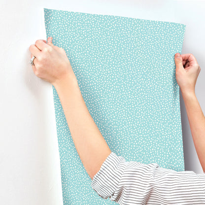 Person in a striped sleeve holds up a light blue petite polka dot wallpaper sample.