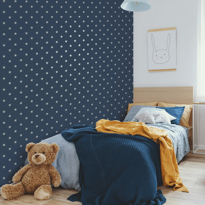 Cozy child’s room with navy star wallpaper, wooden bed, blue bedding, mustard throw, teddy bear, framed bunny art.