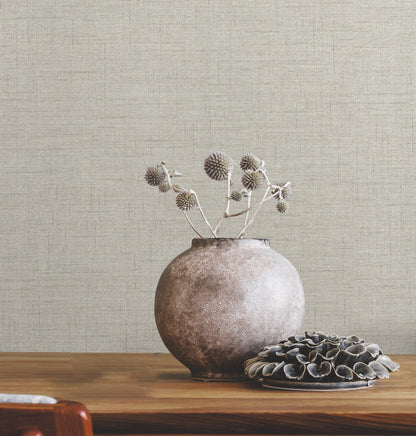 Round ceramic vase with dried thistles on a wooden table, beside a plate of dark shells, beige textured wall backdrop.