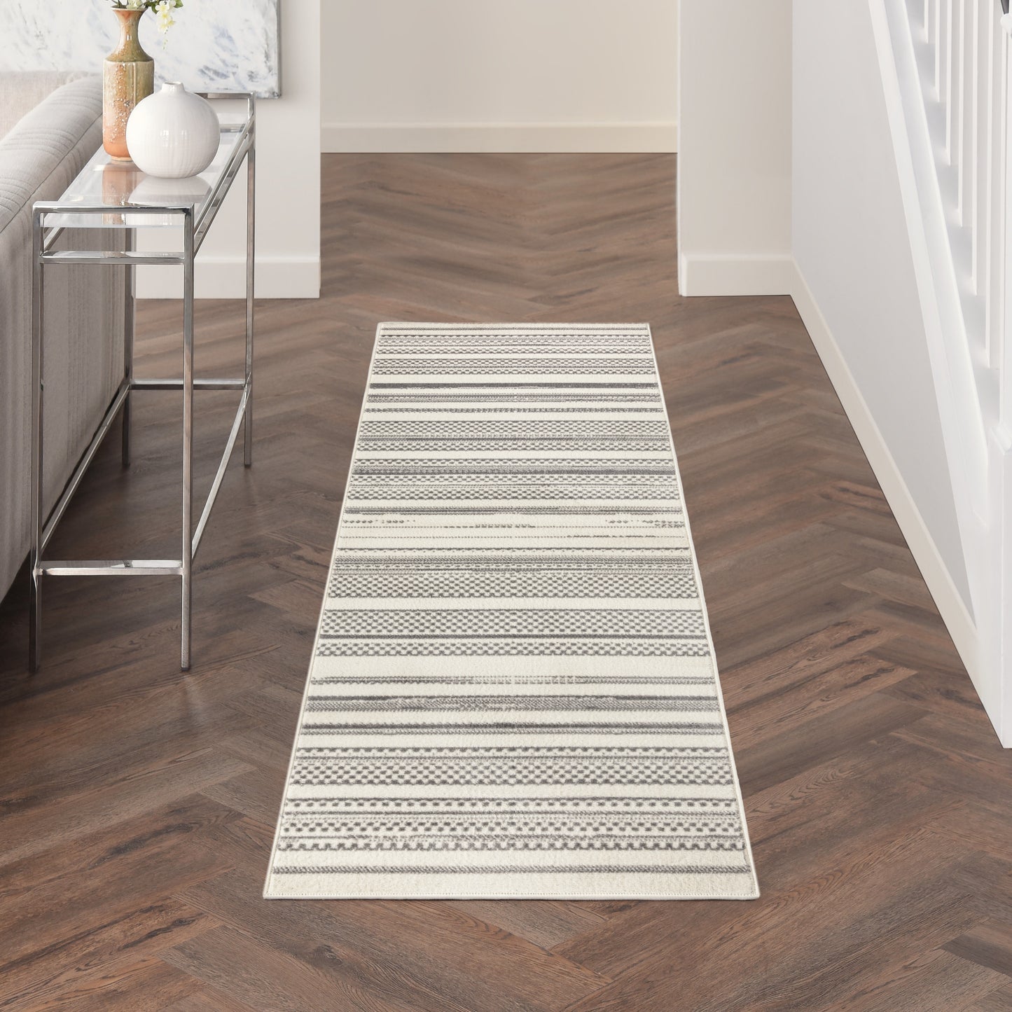 Neutral striped hallway runner rug with geometric patterns in cream, gray and beige on dark wood floor.