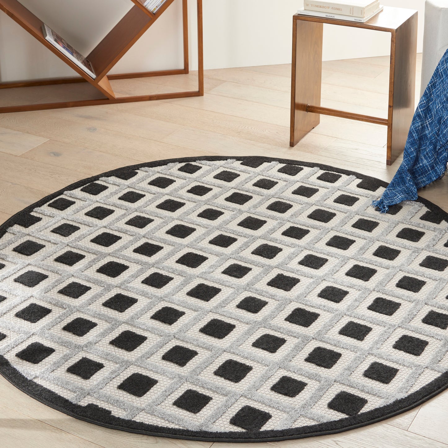 Round rug with light grey background and black square grid pattern, plush texture, in a modern living room.