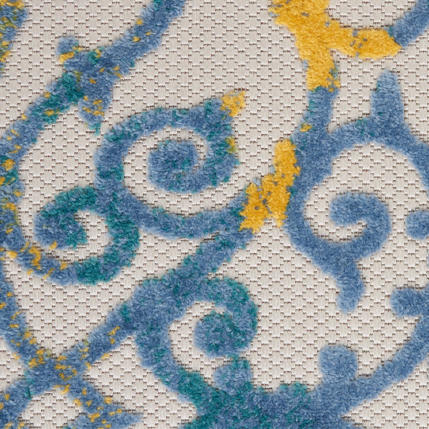 Close-up of textured woven rug with blue and teal damask scrolls and yellow accents on pale beige background.