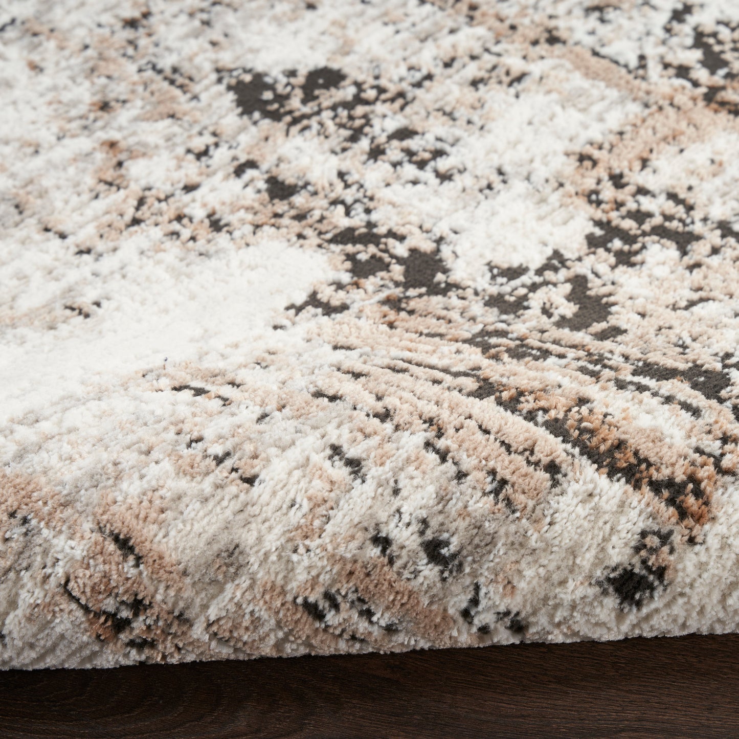 Abstract beige, tan and brown shag rug with plush pile and folded edge on dark wood floor.