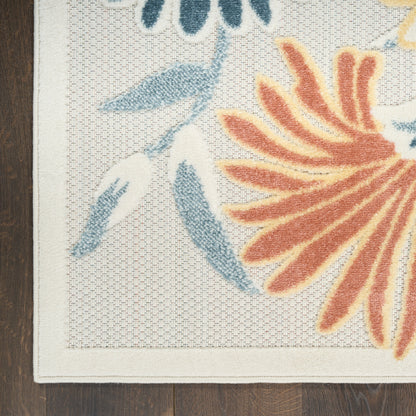 Close-up of a beige outdoor rug with orange flower petals and blue leaves, cream border, on a dark outdoor deck.