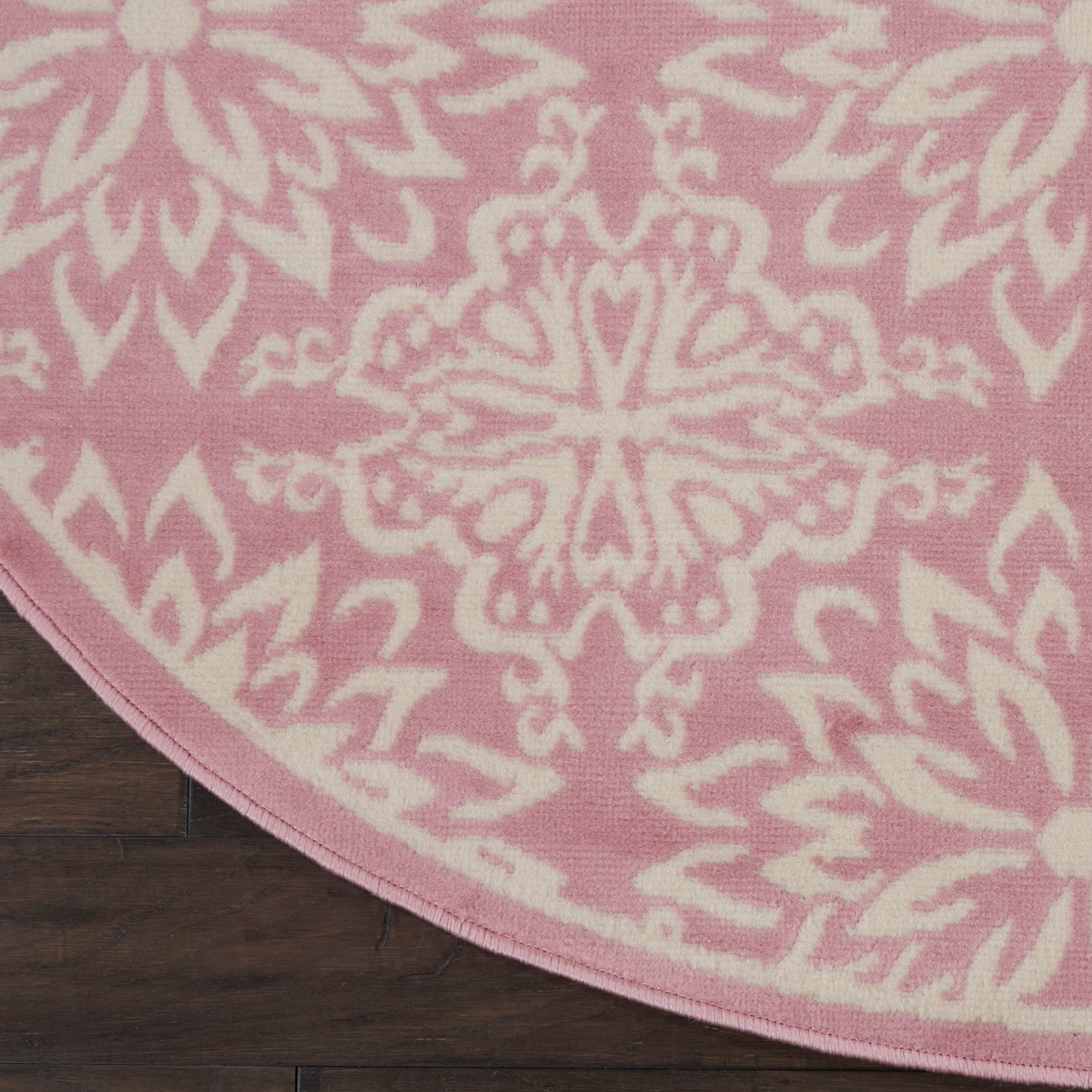 Round pink rug with a white ornate mandala medallion pattern on a dark wooden floor.