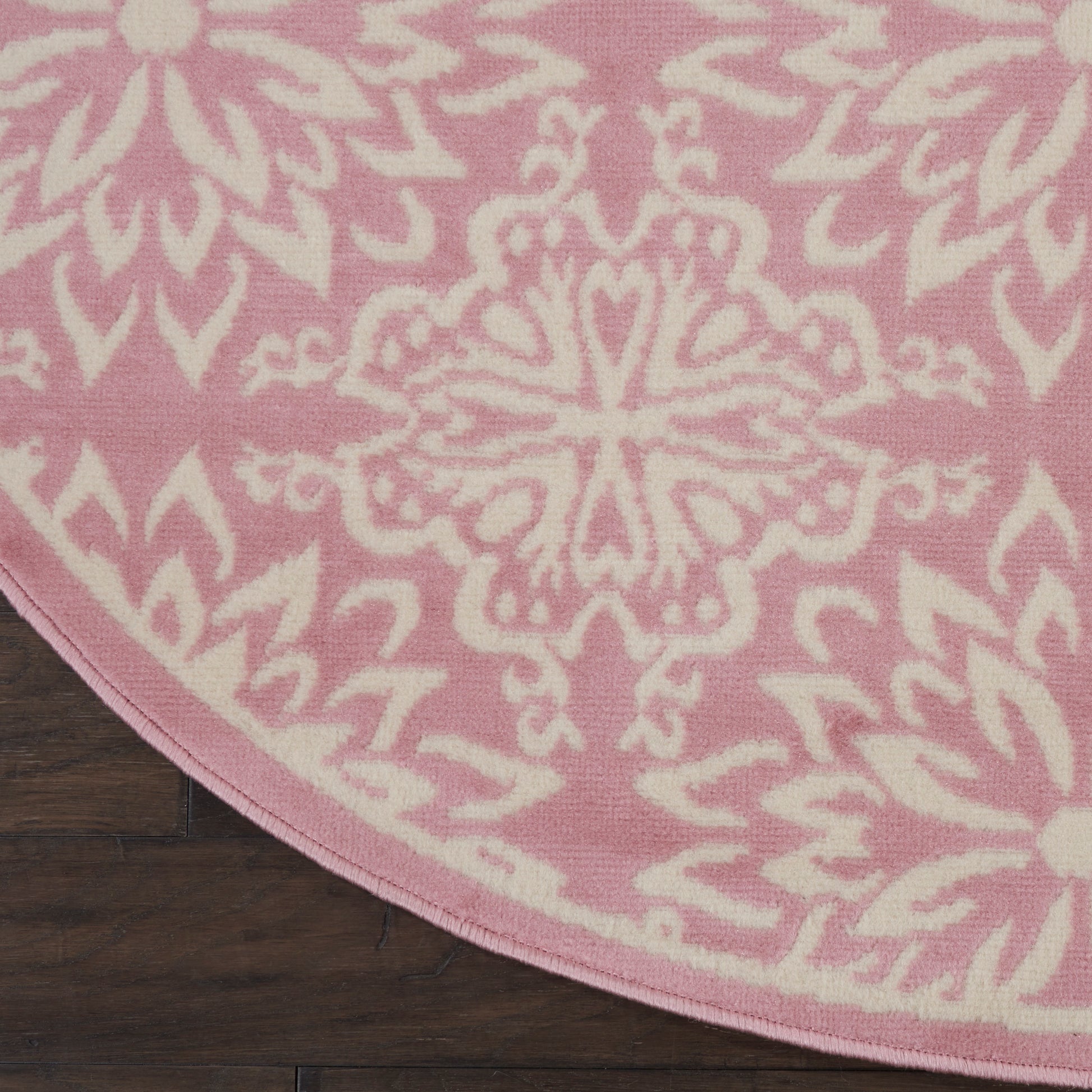Round pink rug with a white ornate mandala medallion pattern on a dark wooden floor.