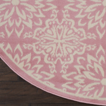 Round pink rug with a white ornate mandala medallion pattern on a dark wooden floor.