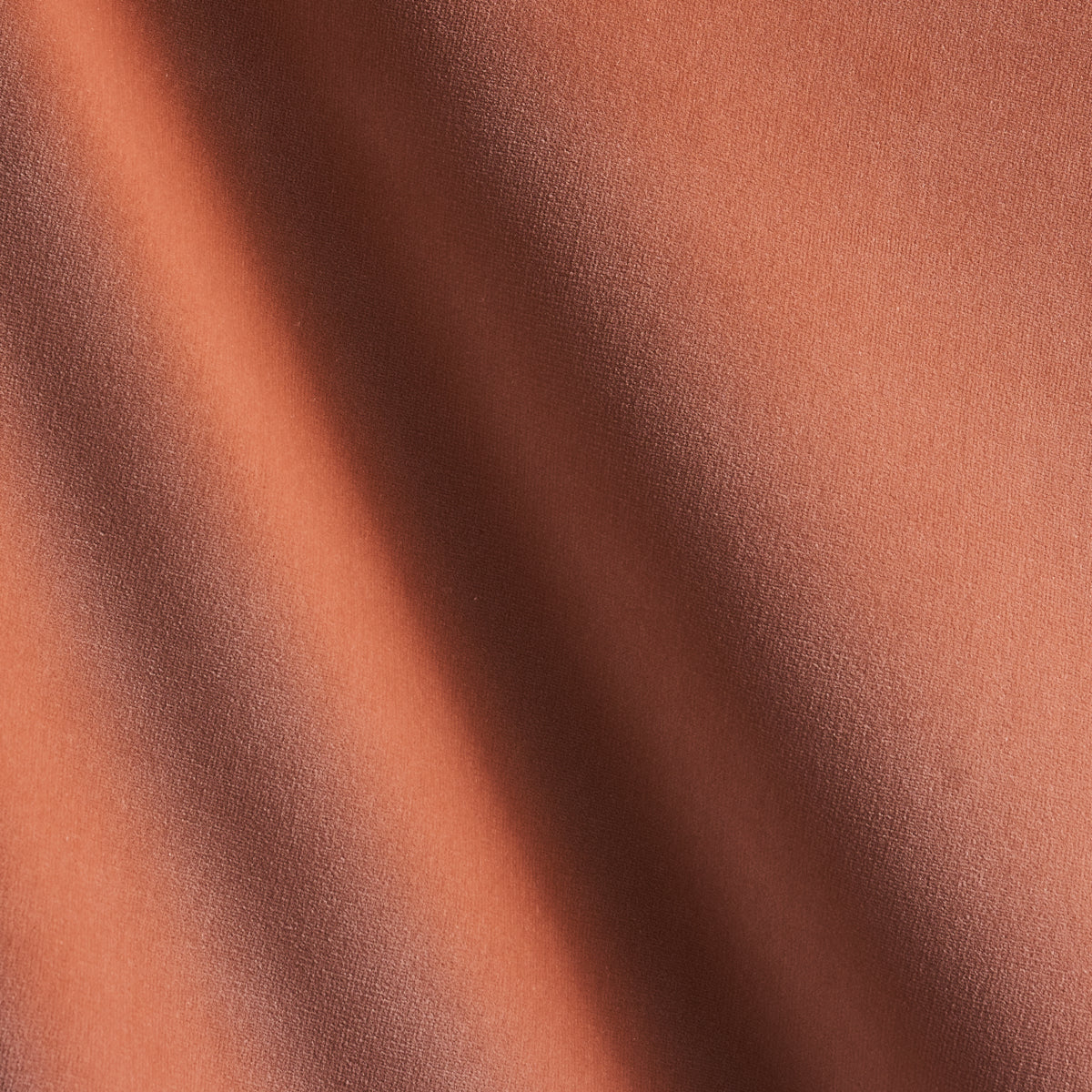 Close-up of burnt orange fabric with diagonal shadows and a soft matte texture.
