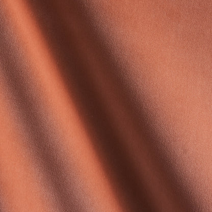 Close-up of burnt orange fabric with diagonal shadows and a soft matte texture.