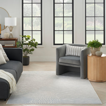 Light-gray patterned area rug in a modern living room with gray sofa and curved armchair.