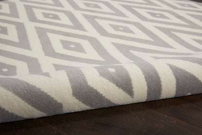 Grey round rug with white geometric diamond pattern, rolled edge, plush pile on dark wood floor.