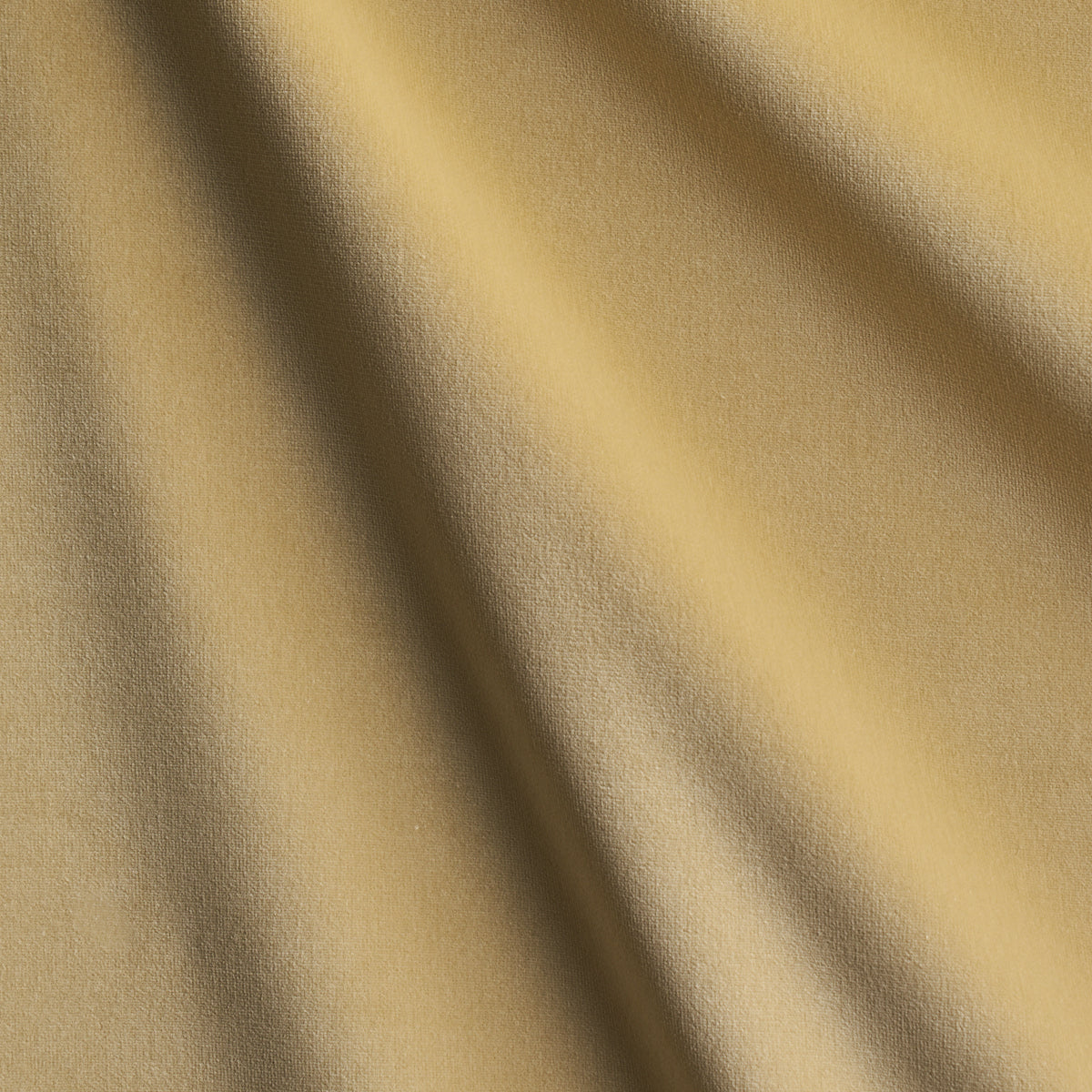 Soft golden-beige fabric with diagonal drapes and subtle texture; close-up textile detail.