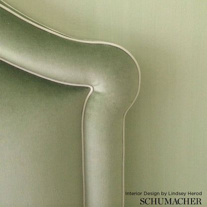 Rounded sage green velvet sofa arm with white piping and curved silhouette.