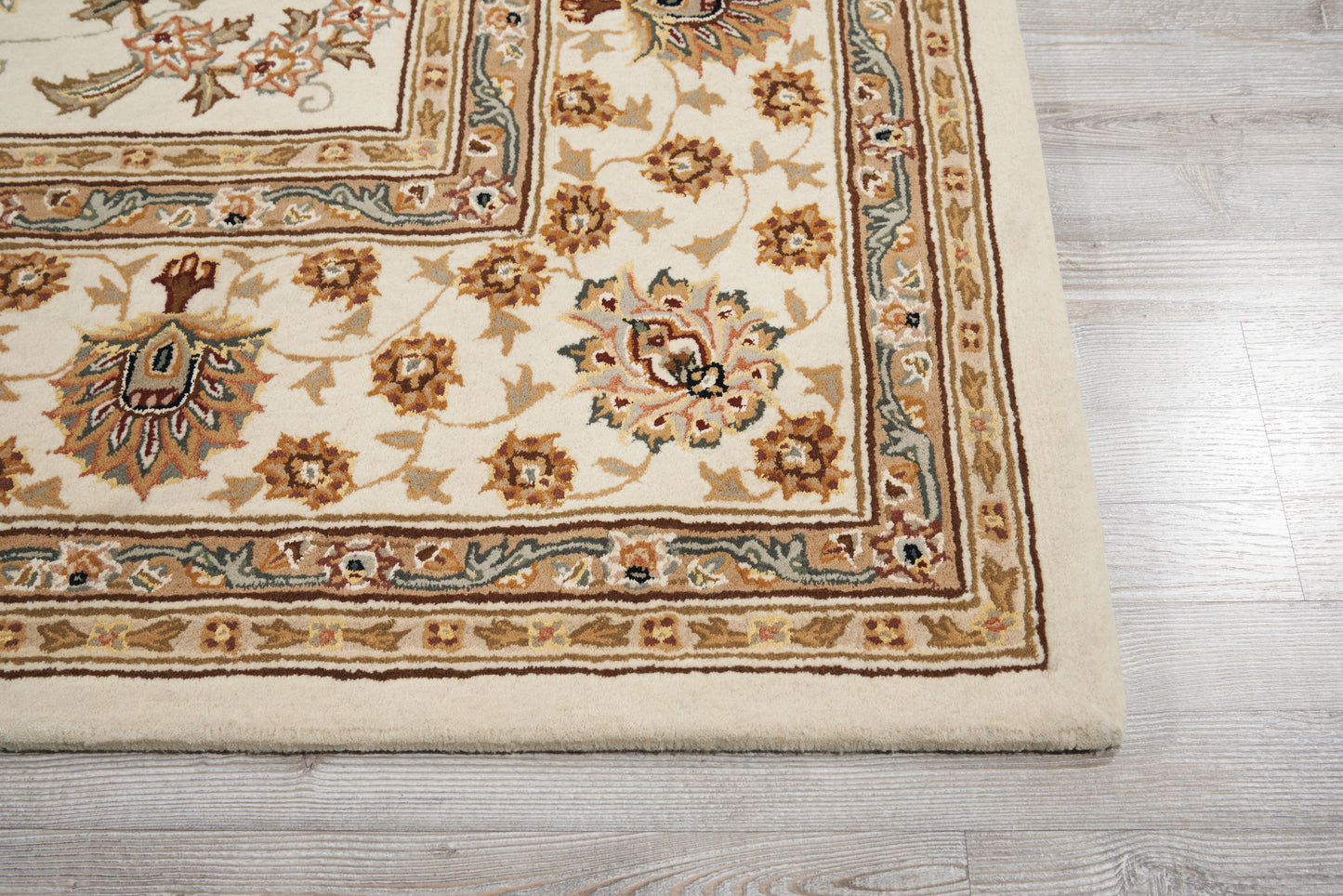 Cream-beige oriental rug with floral motifs and ornate borders in brown and blue on a light wood floor.