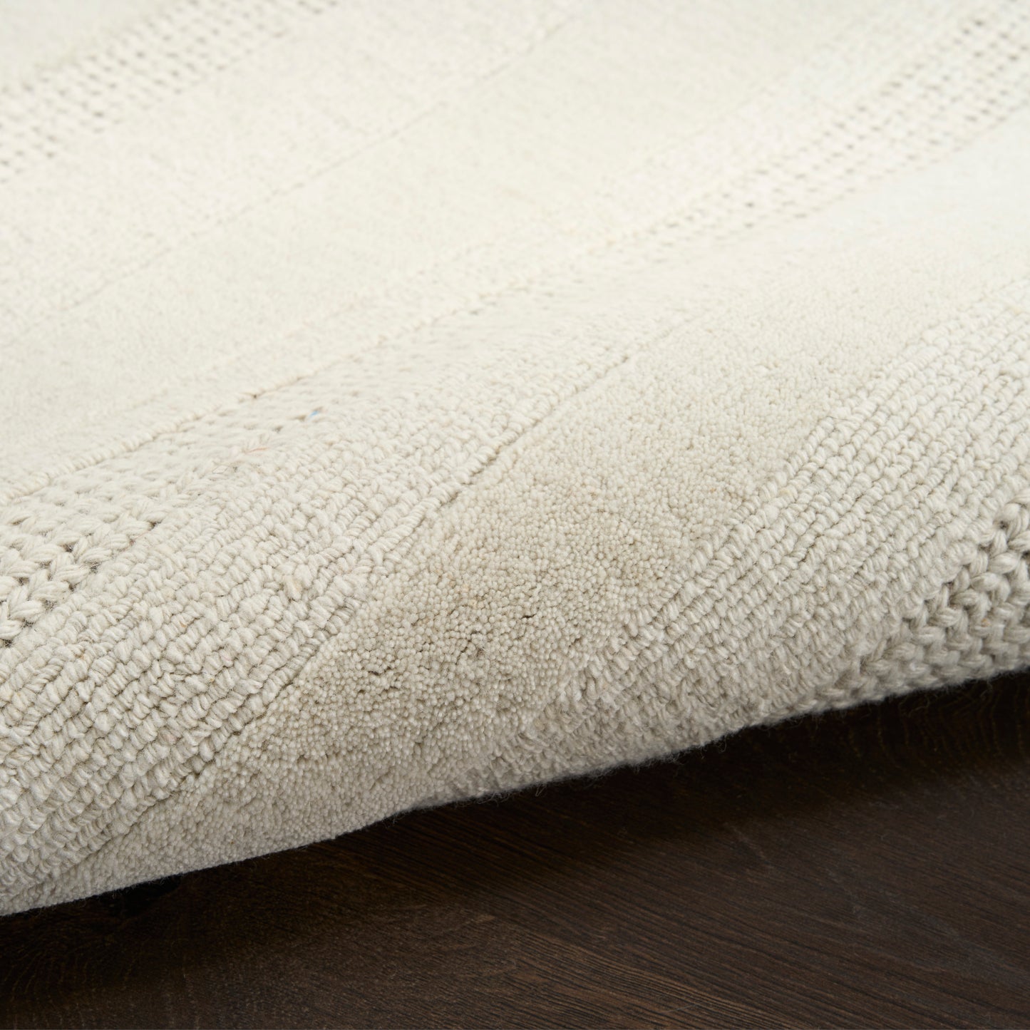 Beige textured rug with plush loop pile and subtle striped pattern, folded on dark wood floor.