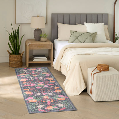 Floral runner rug in pink and peach blossoms with green leaves on a blue gray background beside a beige bed.