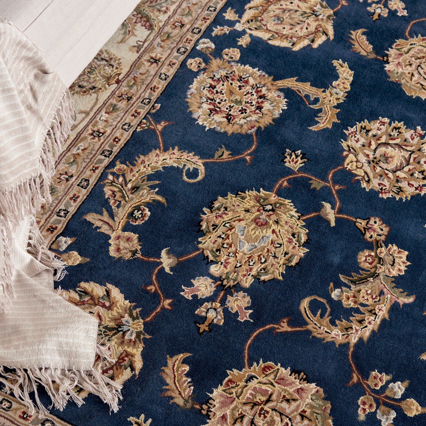 Blue floral area rug with ornate beige and cream vines and a bordered edge, fringed throw partially draped.
