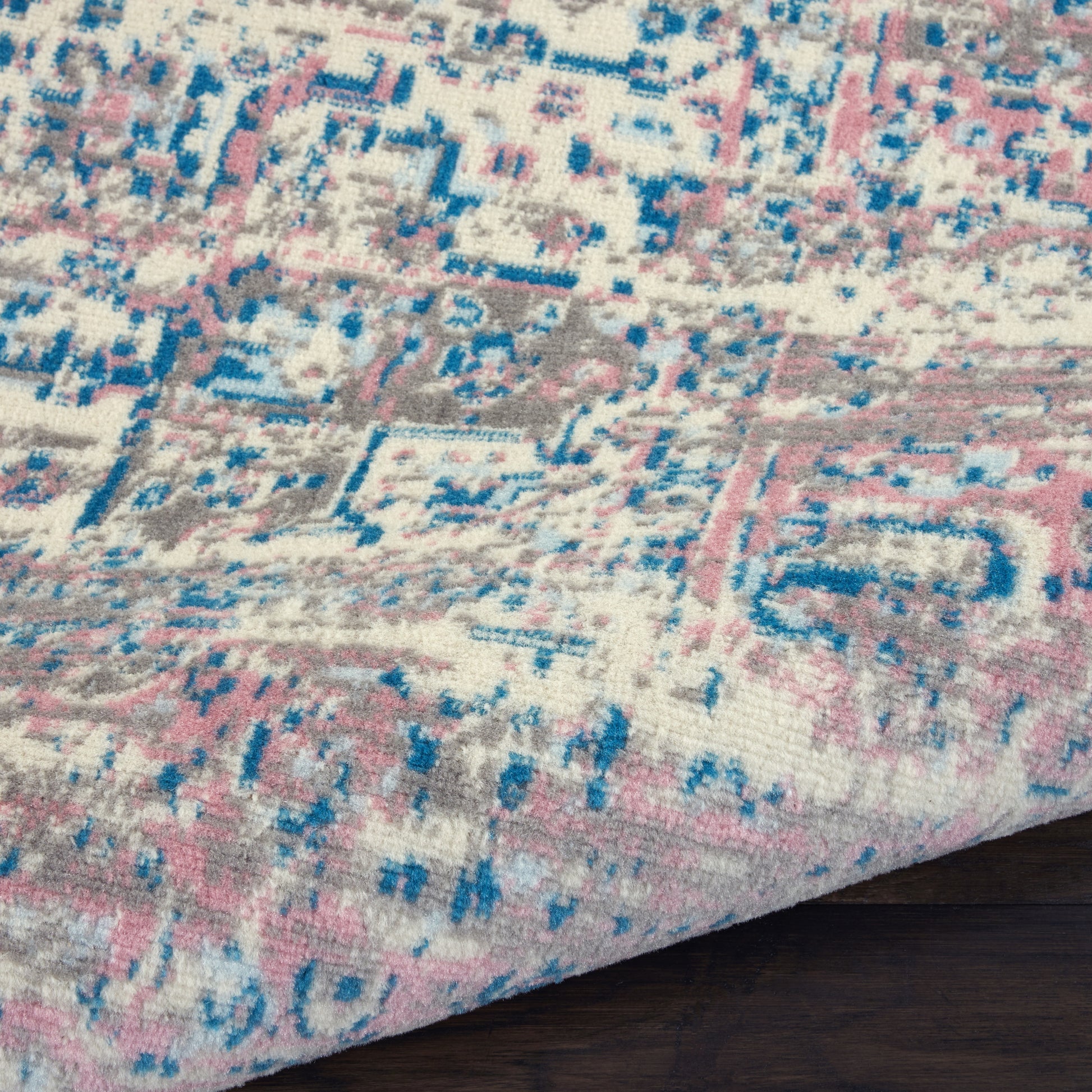 Pastel pink, blue, cream and gray distressed patterned area rug with geometric motifs on dark wood floor.
