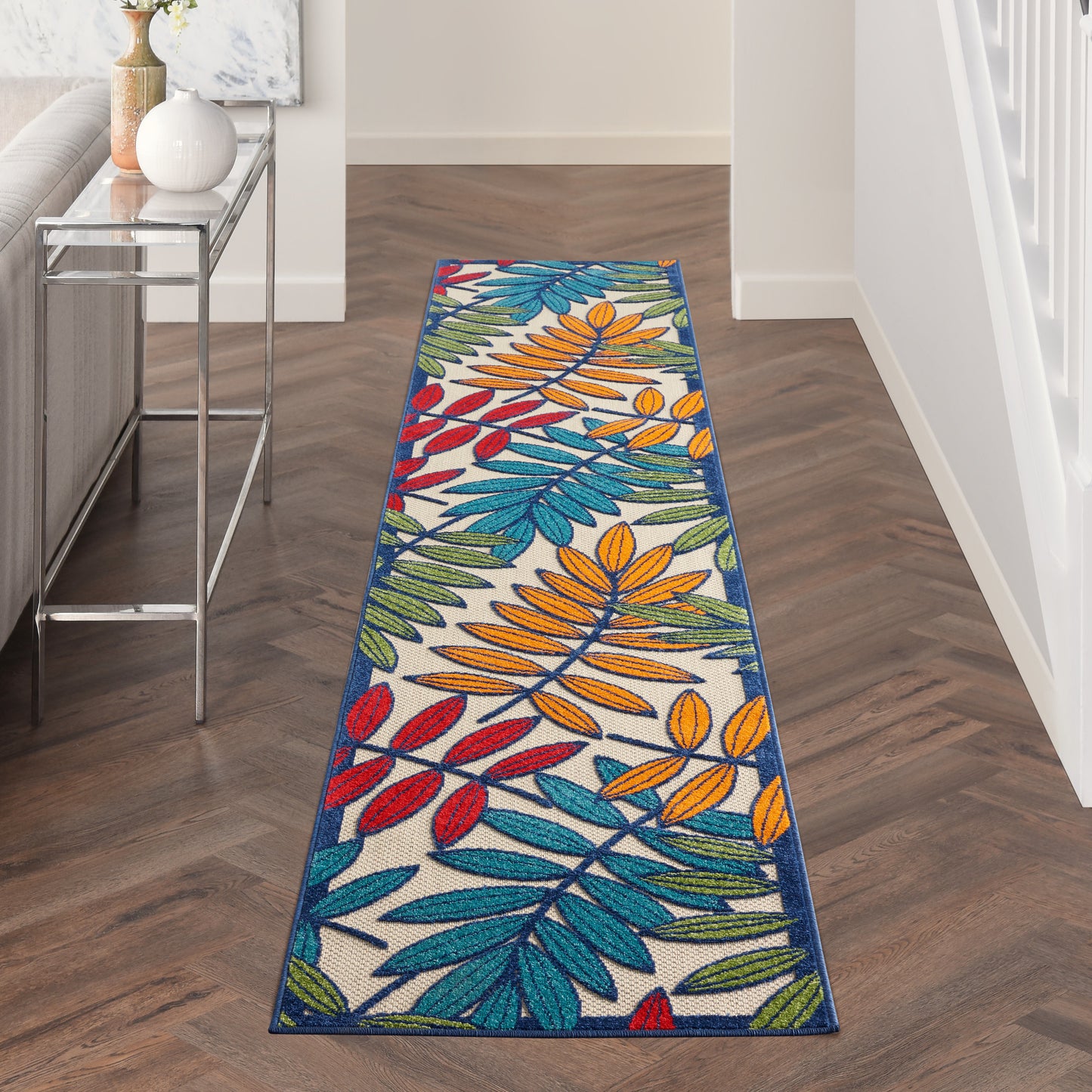Colorful tropical leaf runner rug in blue, orange, red, green on beige; contemporary hallway with blue border.