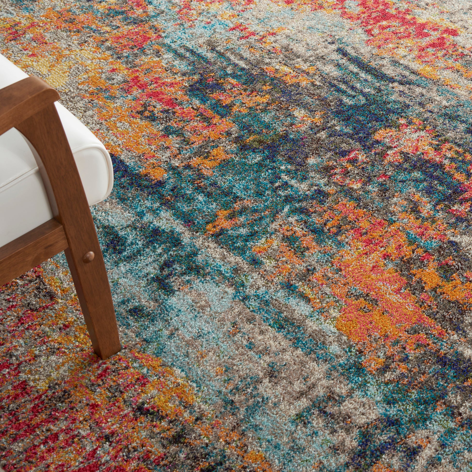 Colorful abstract area rug with teal, blue, orange, pink and gray tones beside a wooden-framed chair.
