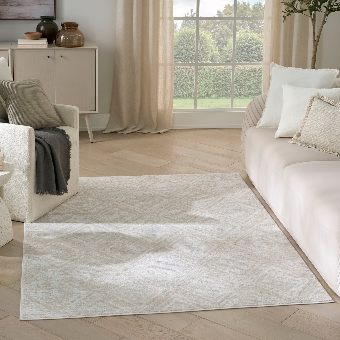 Cream geometric area rug on light wood floor in a neutral living room with beige sofa and layered cushions, 4' x 6'.
