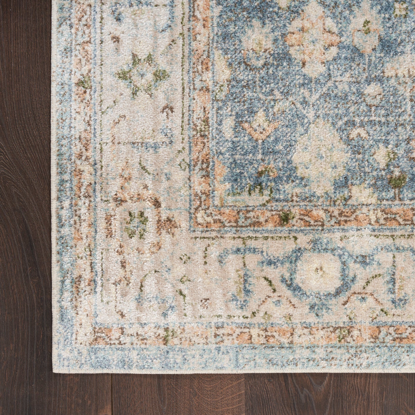 Blue and ivory distressed floral area rug with peach border on dark wood floor.