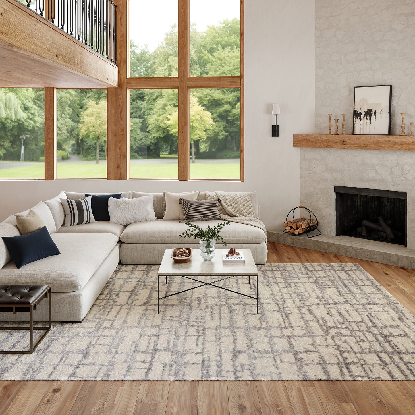 Bright living room with beige sectional, grey rug, large wood-framed windows, and a stone fireplace with a wooden mantle.